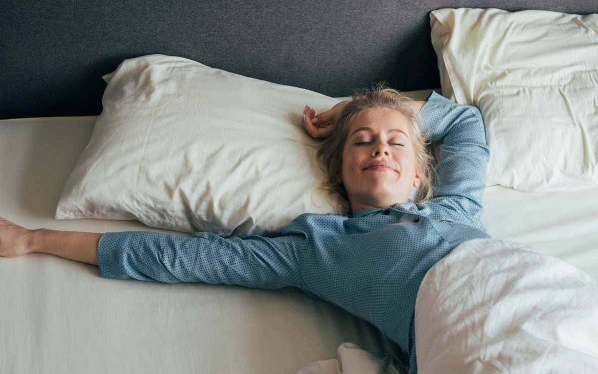 Kvinne som ligger i nyvasket sengetøy. Foto